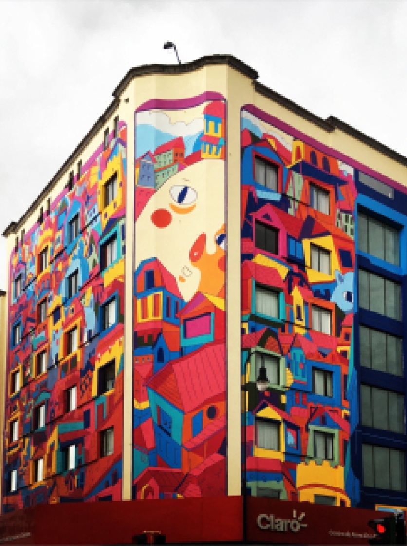 Colorful mural of stacked houses and a large stylized face covering the corner of a building.